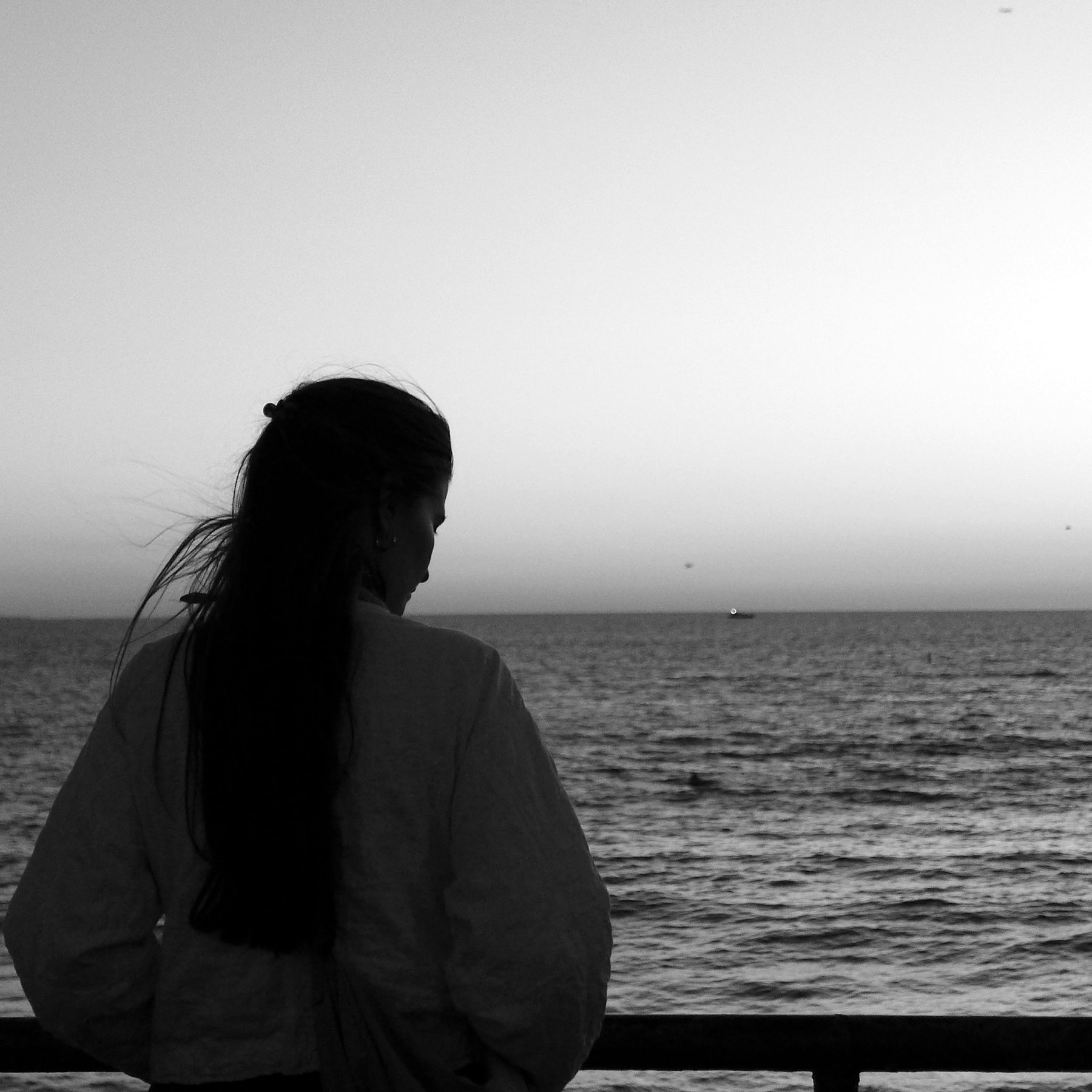 A lone figure seated in silhouette against a stormy sky